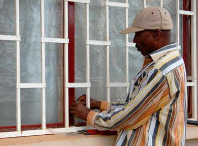 Napoleon covers the windows of the Total Health Center with plastic to block the dust of the dry season.